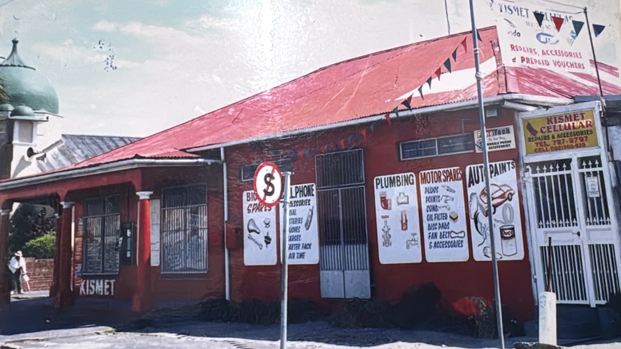 Older photo of Kismet's iconic red building on the Wynberg corner with hand-painted plumbing, motor spares and auto paints signage